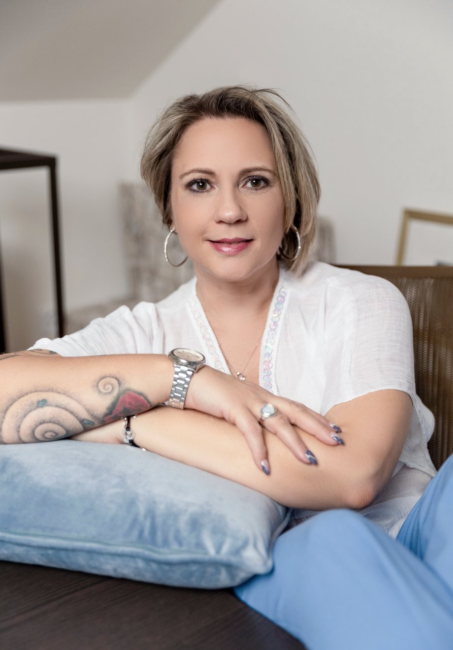 Angelika Stempfle sitzt auf der Couch, die Arme auf einem Kissen verschränkt, und lächelt in die Kamera