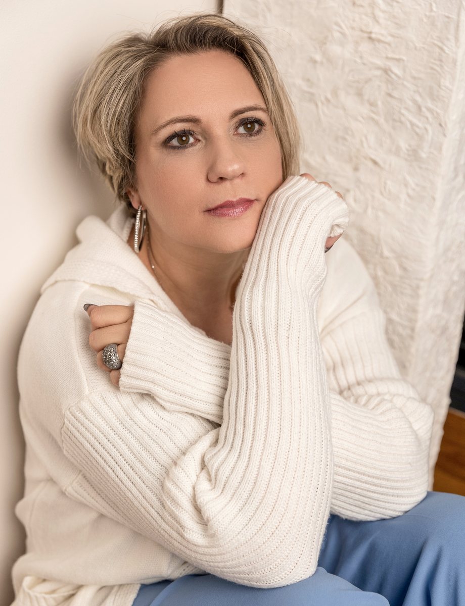 Angelika Stempfle im weißen Strickpullover, das Kinn auf die Hände gestützt, nachdenklicher Blick