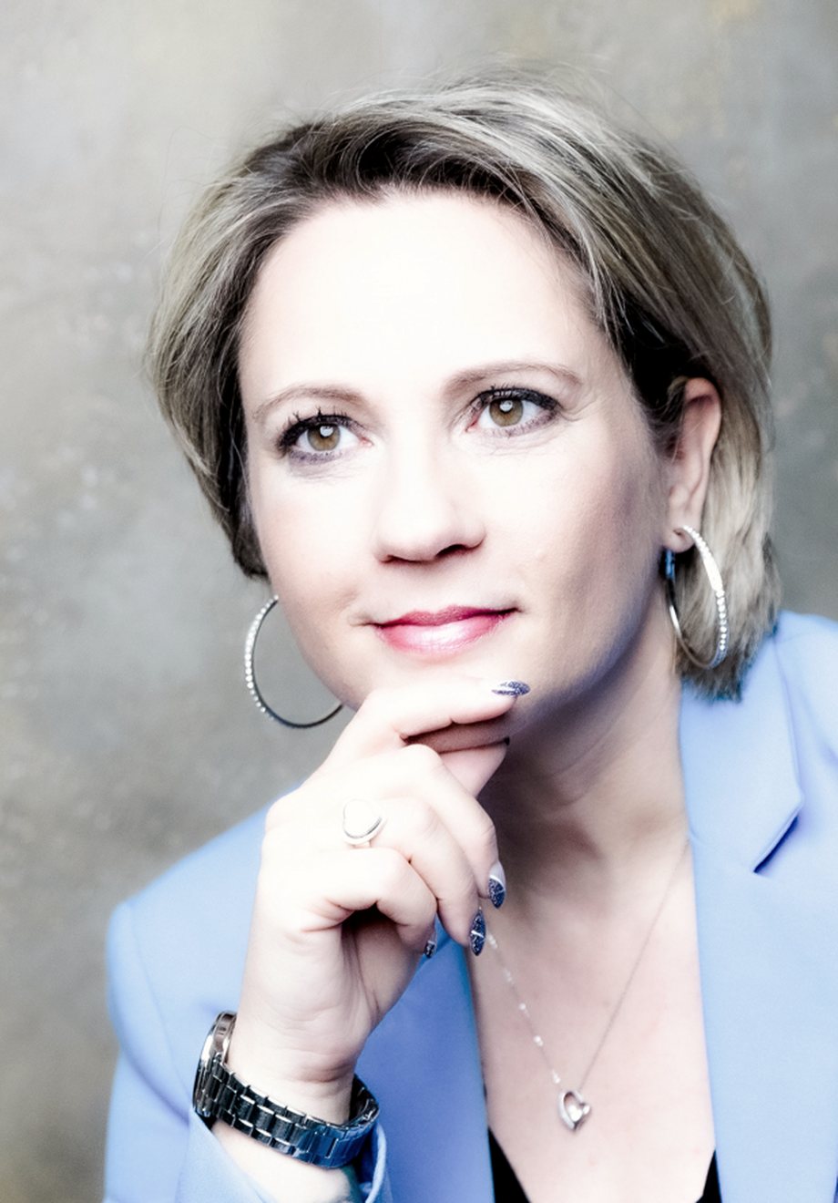 Angelika Stempfle im hellblauen Blazer, die Hand am Kinn, aufmerksamer Blick